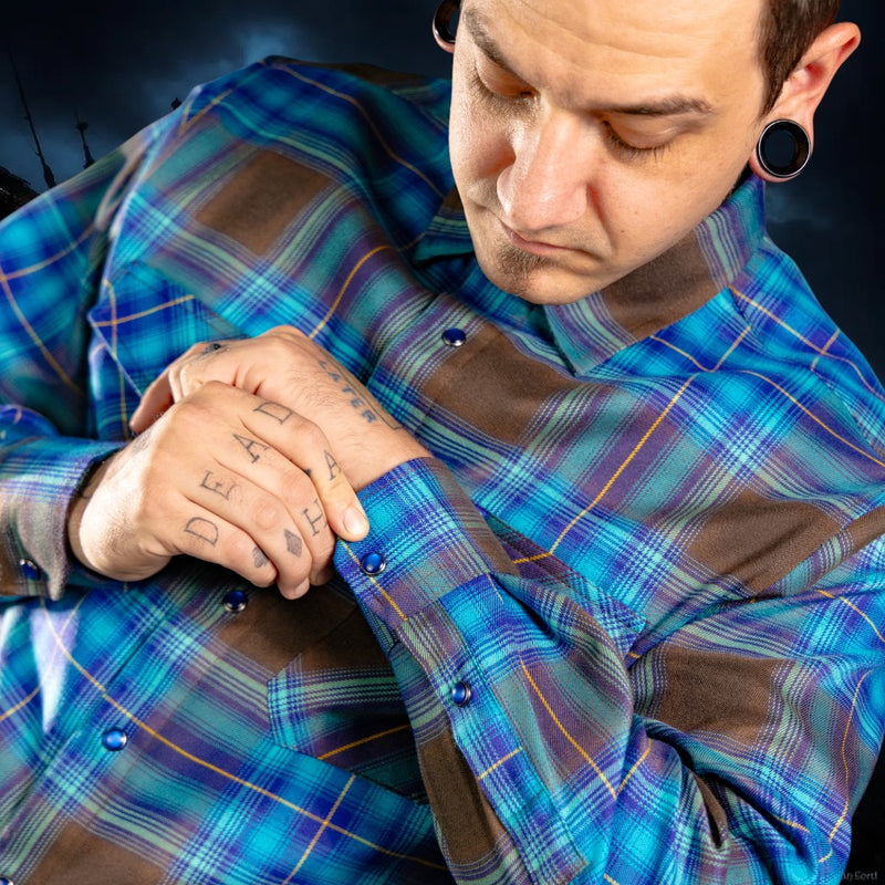 Person wearing a blue plaid shirt with tattoos on their arms.